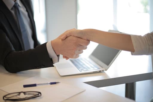 Photo of two people shaking hands over a desk with a laptop representing working with a car accident lawyer in Kansas City at Sloan Law Office, LLC